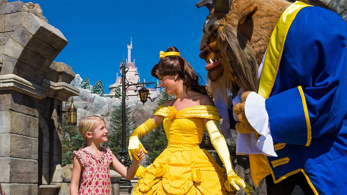 little girl holding Belle's hand with the Beast standing nearby in Fantasyland in Orlando, Florida, USA