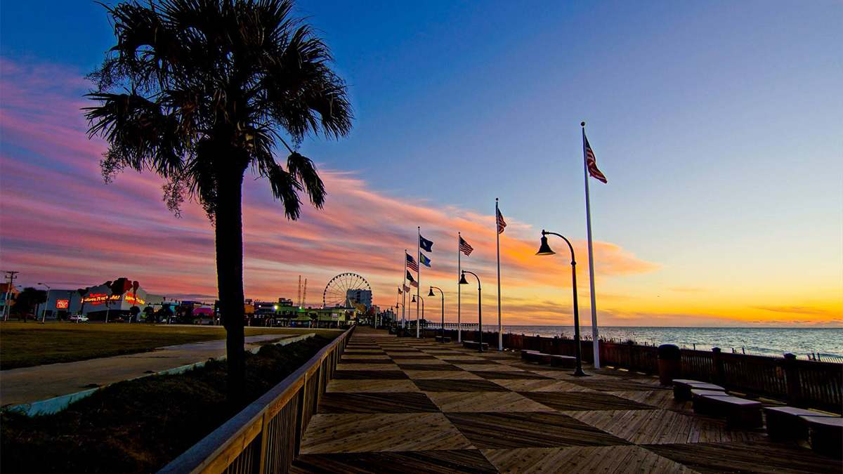 ground view of the flags ferris wheel along the boardwalk with the sun setting behind the ocean in Myrtle Beach, South Carolina, USA