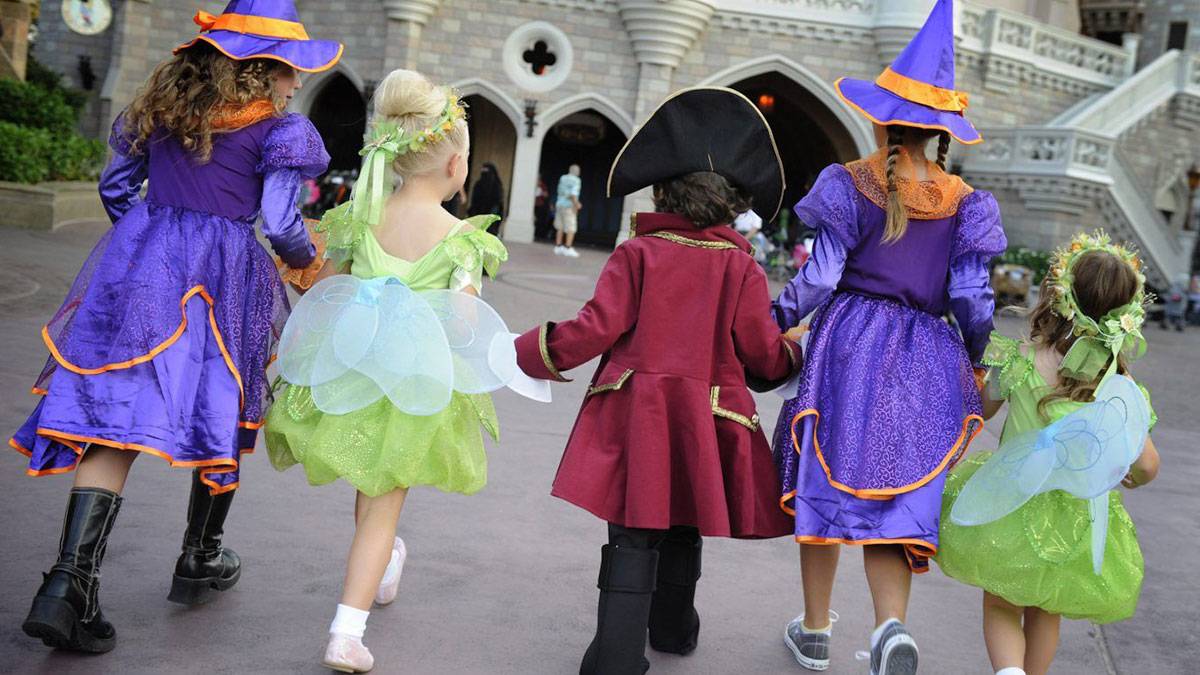 small children holding hands with halloween costumes walking towards Cinderella Castle inside Walt Disney World in Orlando, Florida, USA