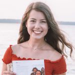 michaela smiling holding magazine with body of water in background