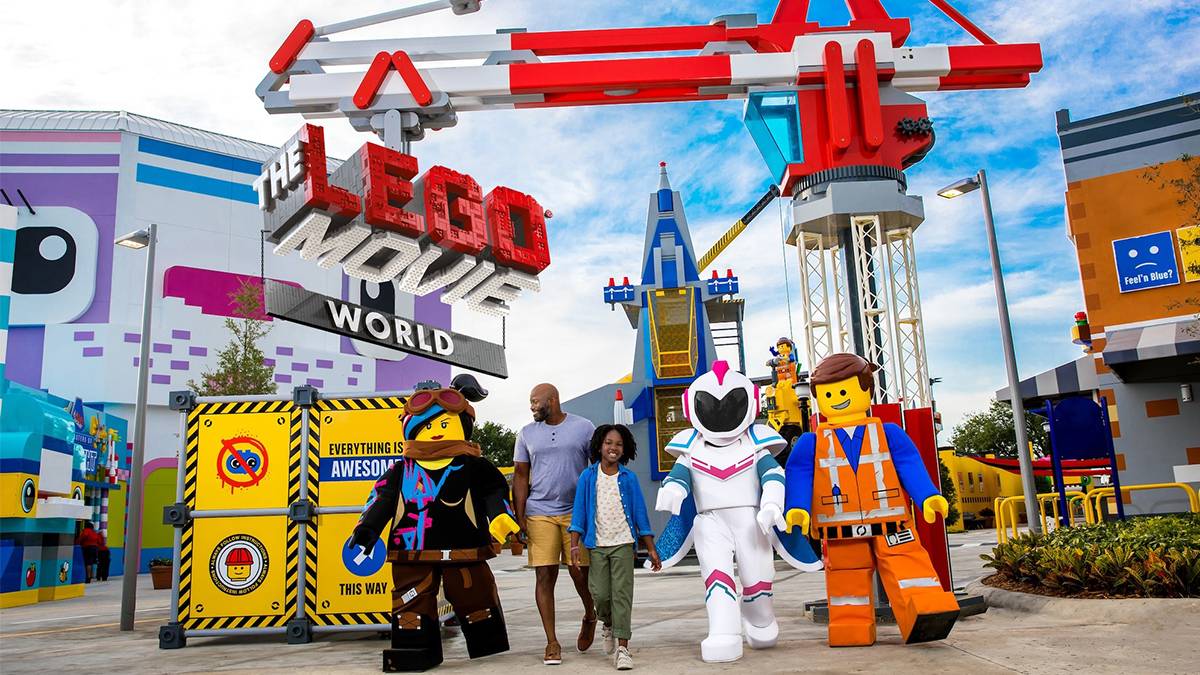 Father and daughter walking with LEGO figures with the theme park behind them and a blue cloudy sky in San Diego, California