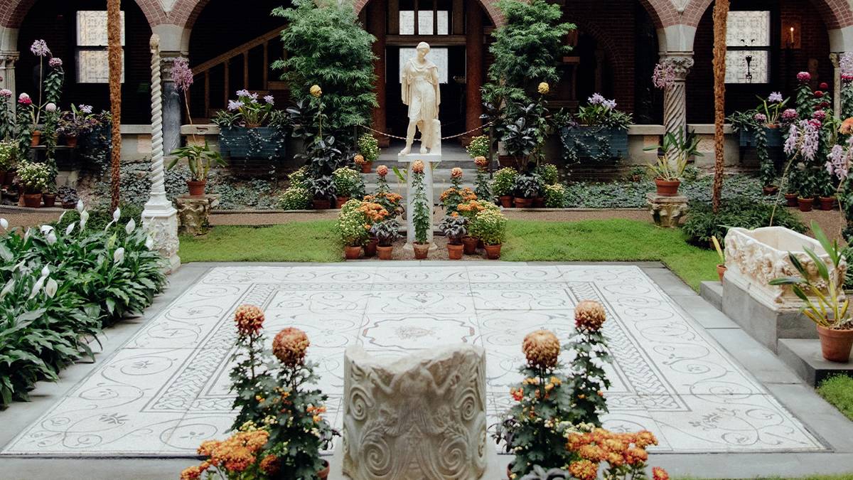 A courtyard with lots of bushes and flowers with a stone patio in the middle and a statue in the background in Boston, Massachusetts