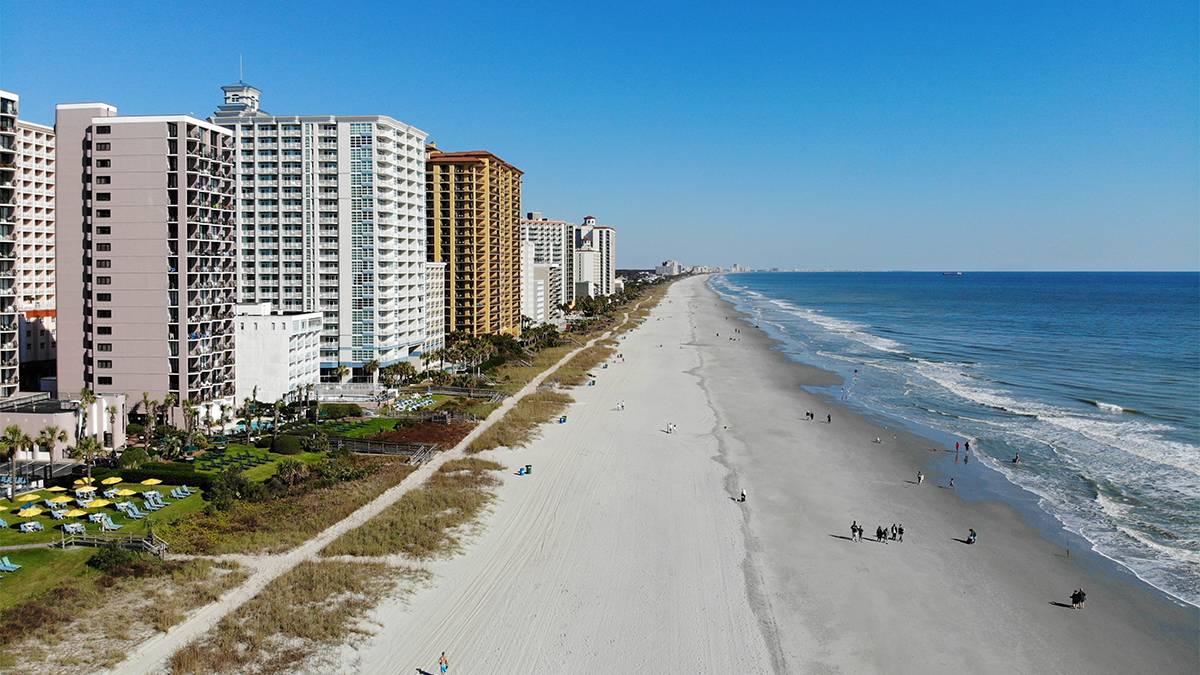 Aerial view of Myrtle Beach with the ocean on your right and a string of hotel on the left on a sunny with a few people scattered on the beach