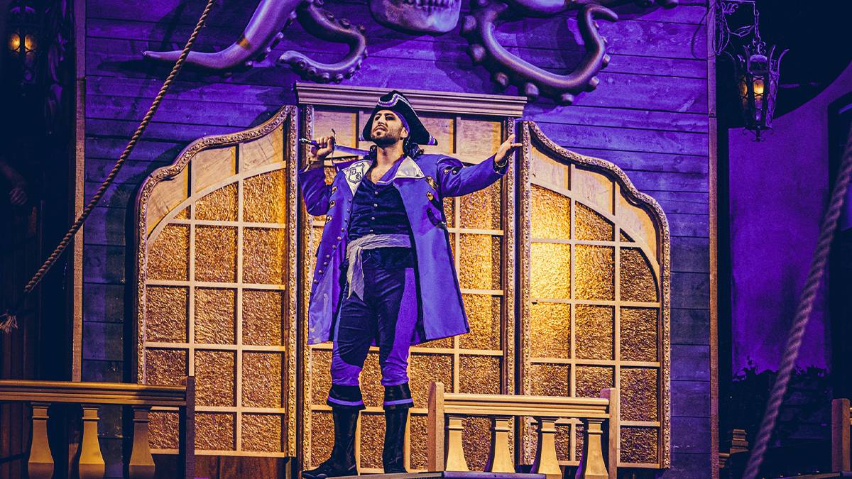 Pirate dressed in an all purple outfit standing on the deck of a ship with a sword over his shoulder at the Pirates Voyage Dinner and Show in Myrtle Beach, South Carolina, USA