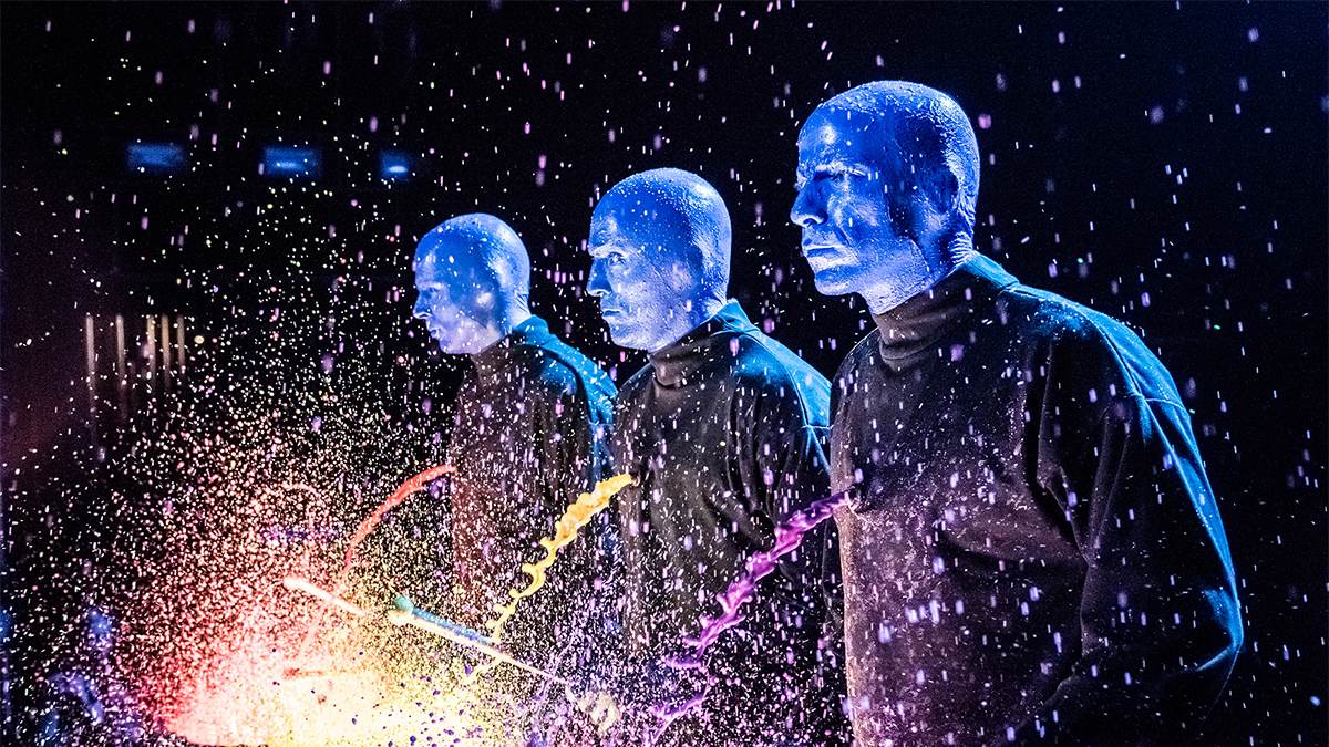 Blue Man Group playing drums with red, yellow, and purple paint on them in concert in NYC, New York