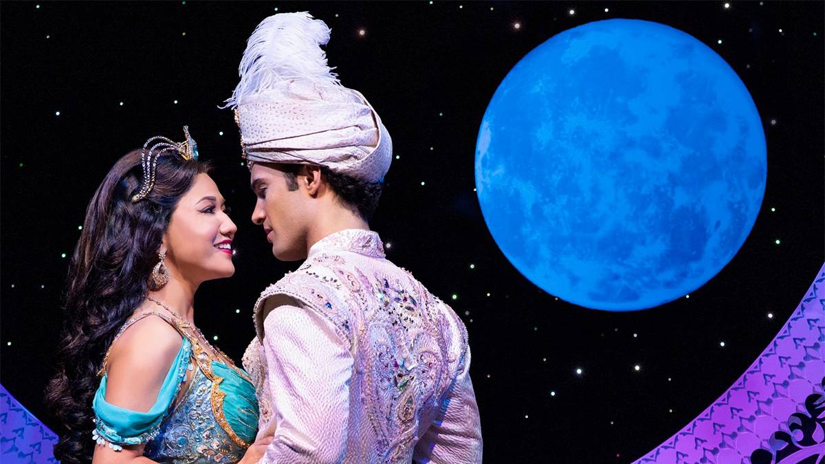 Close up photo of Jasmine and Aladdin about to kiss with a blue moon behind them on Broadway in NYC, New York, USA