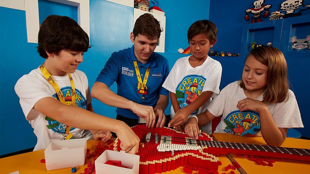 Three kids in white shirts and a lego employee building a red lego guitar in San Francisco, California