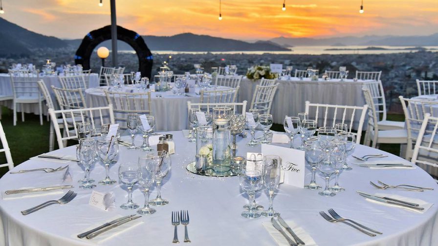 A round table with a white cloth set for several people to dine at it with a beautiful orange sunset behind it at Sundial Restaurant + Bar in San Francisco, California, USA