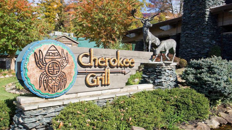 Close up of a wooden sign with a tribal symbol on the left side and deer statues on the right and gold letting that says Cherokee Grill in Gatlinburg, Tennessee, USA
