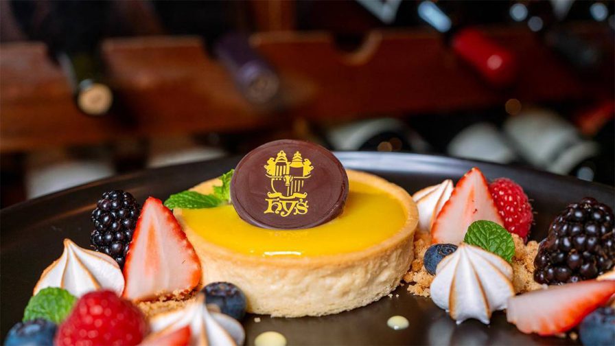 Close up photo of a lemon tart surrounded by fruit with a chocolate circle that have the logo for Hy's Steak House printed on it in gold in Honolulu, Hawaii, USA