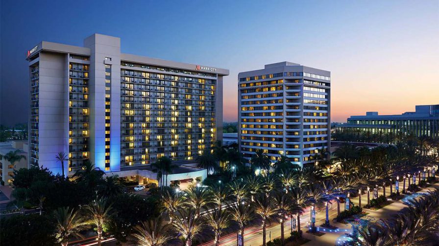 Wide shot of the Anaheim Marriott at sunset with the road lined with palm trees in front of it in Los Angeles, California, USA