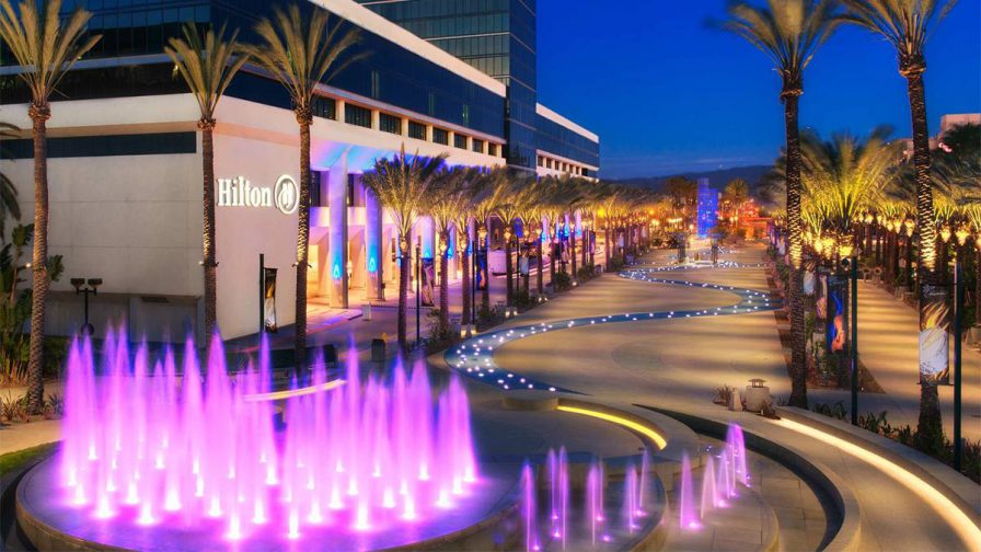 The Hilton Anaheim with a large purple lit water feature in front of it and palm trees lining the entrance in Los Angeles, California, USA