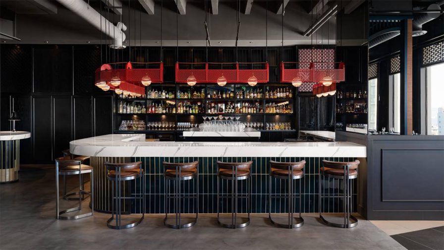 A bar right a white counter top and leather stools plus red caged light fixtures hanging above the bar at Empress by Boon in San Francisco, California, USA