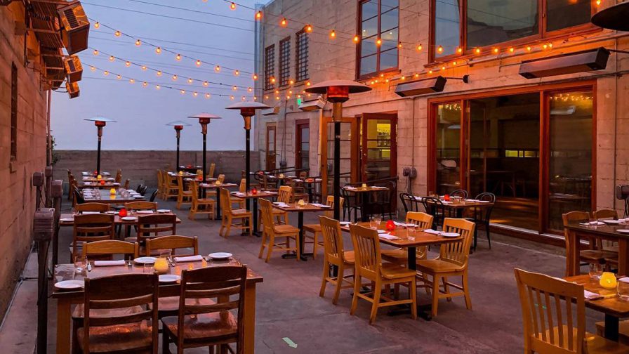 Wide shot of the outdoor dining area with simple wooden tables and chairs and string lights hung above them at Foreign Cinema in San Francisco, California, USA