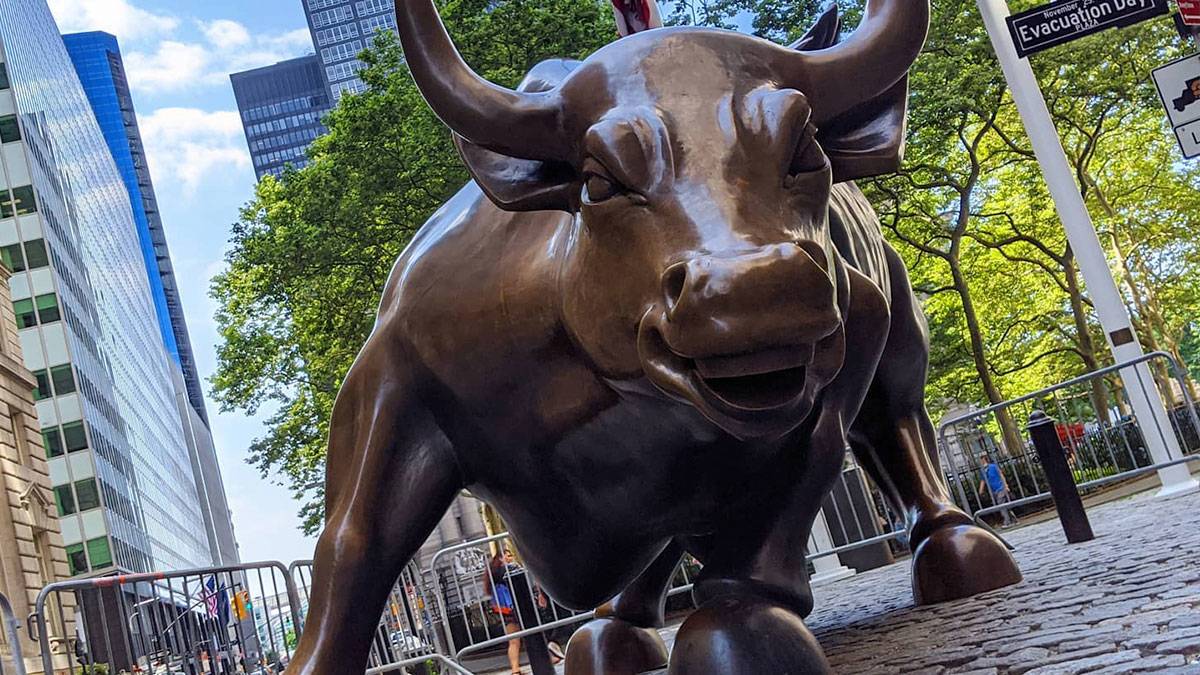 close-up, angled shot of Charging Bull Statue on cobblestone with trees and buildings in the background