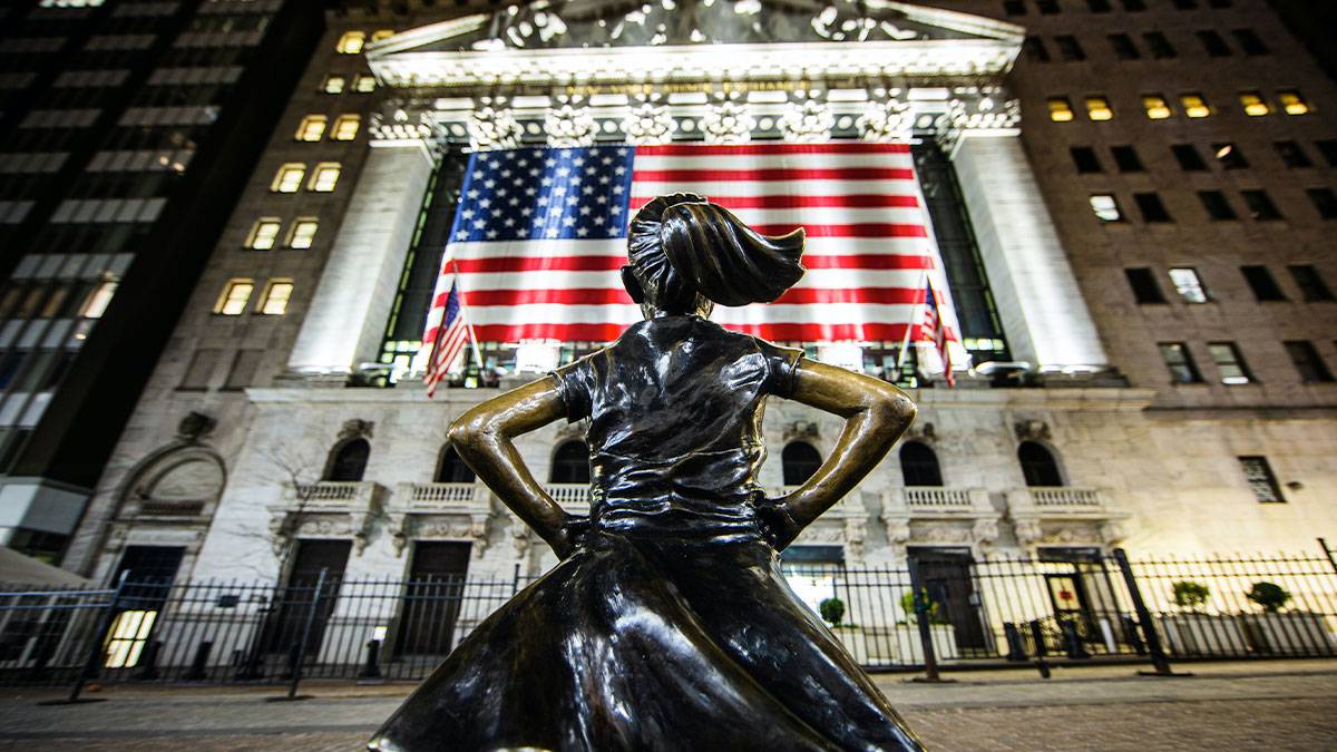 Fearless Girl Statue facing building with American Flag during night in New York City, New York, USA