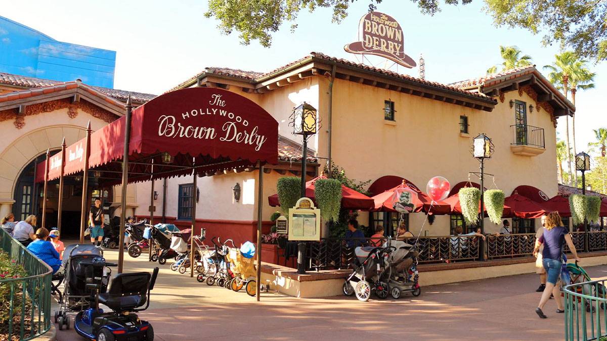 exterior of The Hollywood Brown Derby with strollers lined up at entrance and people dining in outside area in Disneyworld, Orlando, Florida, USA