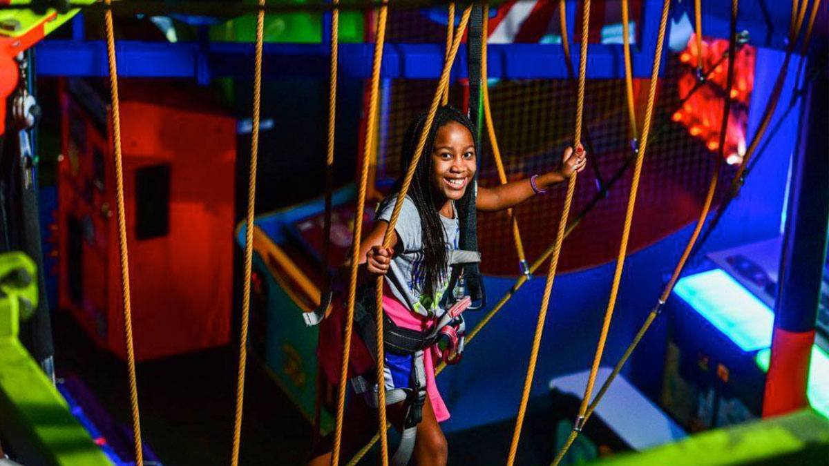 child wearing harness holding on to ropes while going through course at Indoor Ropes Challenge Course in WonderWorks, Orlando, Florida, USA