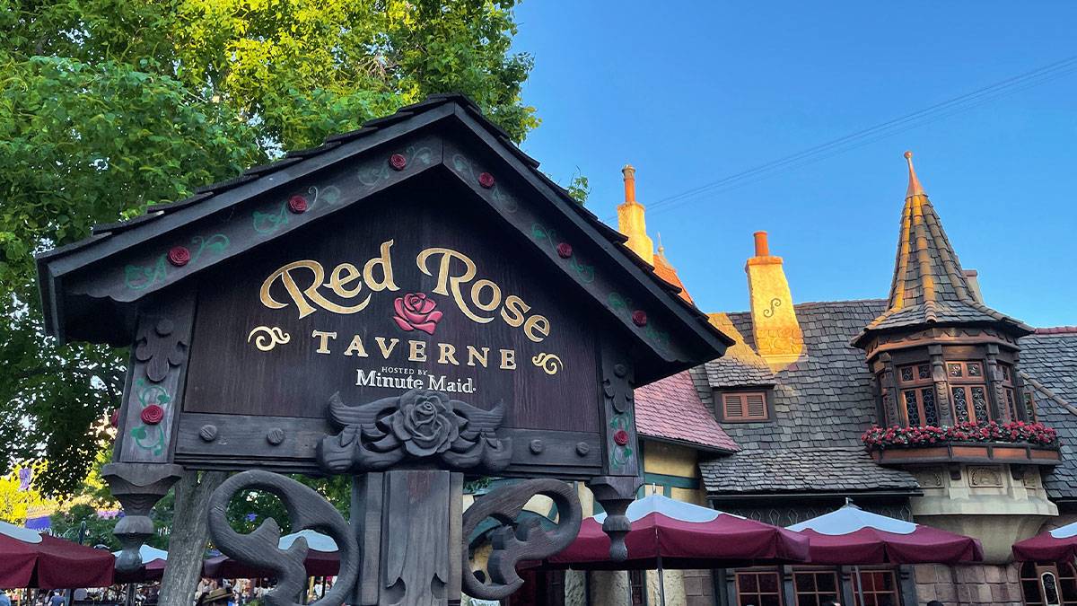 sign board and exterior of the Red Rose Taverne with sunlight casting glow on roof of structure and trees in the background in Disneyland, Anaheim, California, USA