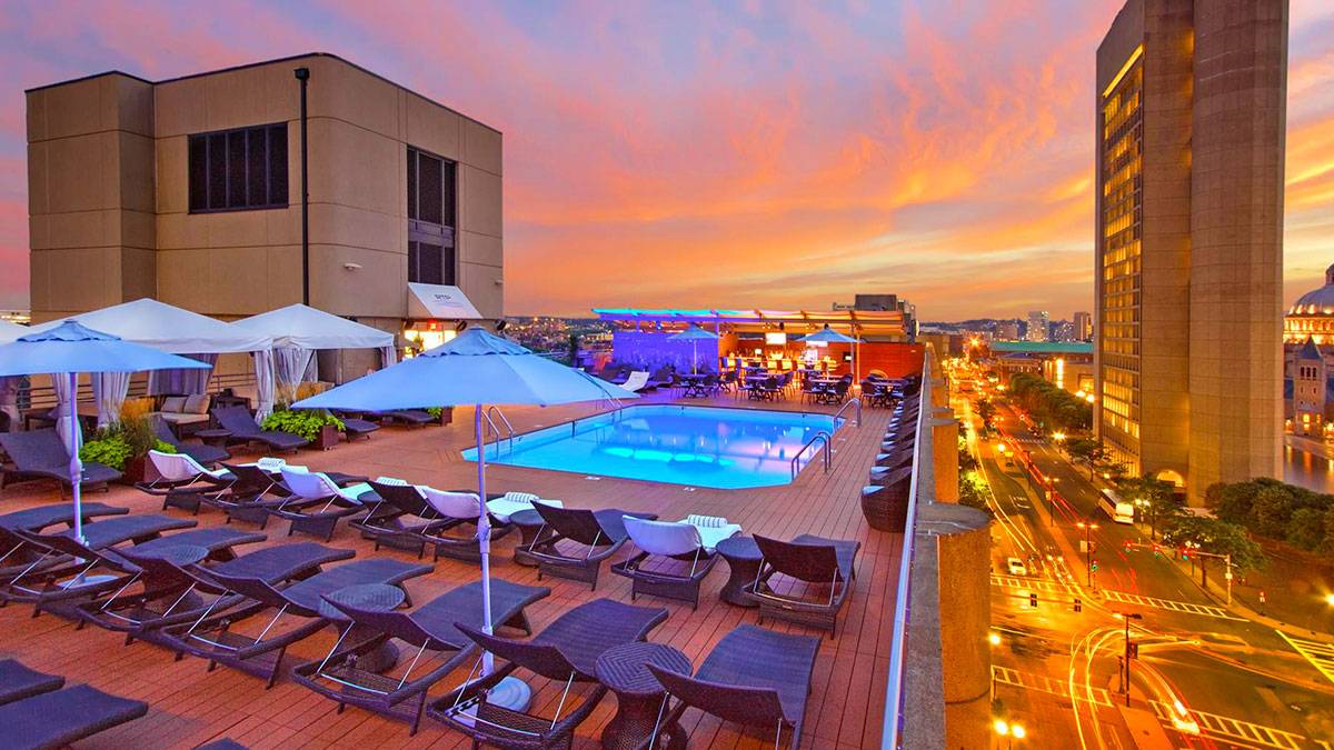 aerial view of rooftop pool of The Colonnade Hotel pool with lounge chairs and umbrellas during sunset with street below and surrounding buildings in Boston, Massachusetts, USA