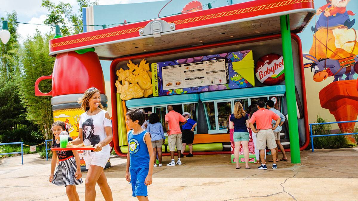 family happily walking away with their meal and people in line in the background in front of Woody's Lunch Box restaurant in Disneyworld, Orlando, Florida, USA