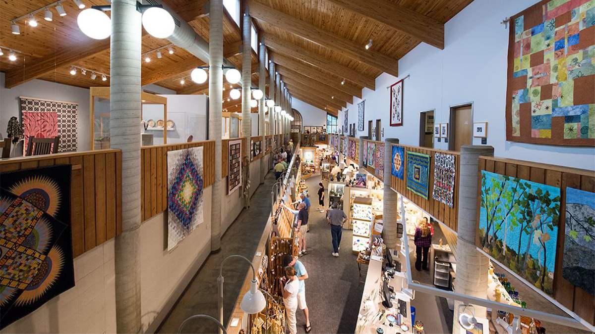 Looking down over the railing at the Southern Highland Craft Guild Folk Art Center with people looking at the exhibits and quilts lining the walls in Asheville, North Carolina, USA