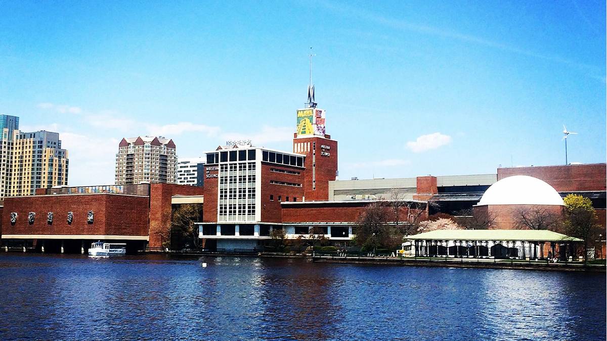 Wide shot of the exterior of the Museum of Science from the water on a sunny day in Boston, Massachusetts, USA