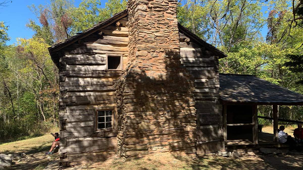 View of the side of the Walker Sisters Cabin with people sitting on the front and back porch on a sunny day in Gatlinburg, Tennessee, USA