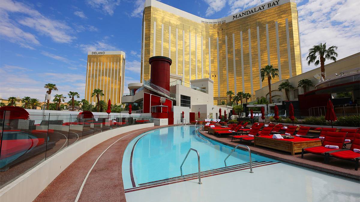View of the Moorea Beach Club at Mandalay Bay with red chairs and lounging areas and a s curved heater pool on a sunny day in Las Vegas, Nevada, USA