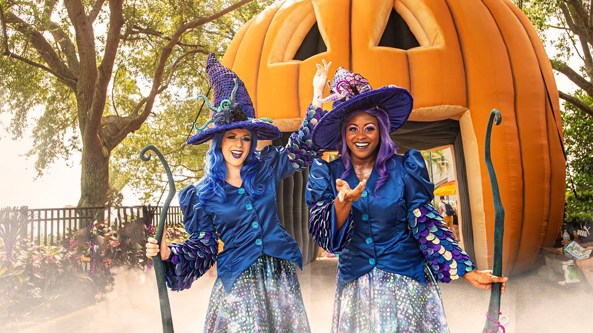 Two women with blue and purple hair in witches costumes standing in front of a giant Jack-O-Lantern for Spooktacular at SeaWorld in Orlando, Florida, USA