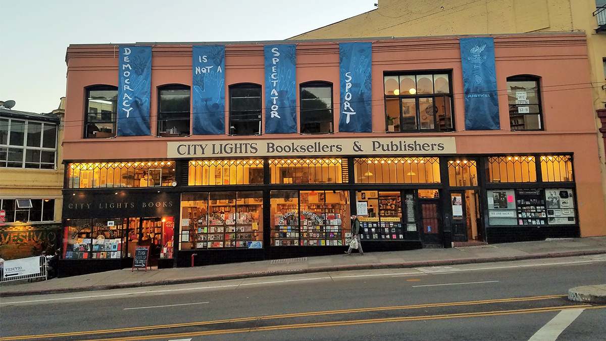 Wide shot of the exterior of City Lights San Francisco in the evening with their lights on inside and you can see books through their tall large windows in San Francisco, California, USA