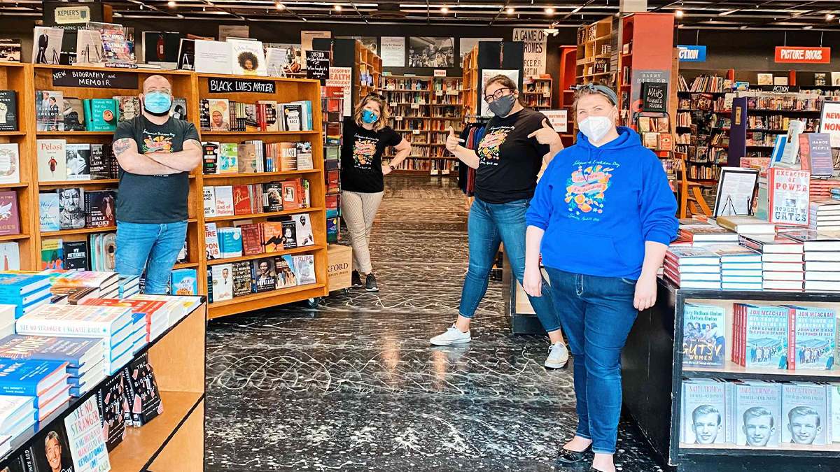 View of four workers standing in Kepler's Books and Magazines with all of the store shelves behind them on a bright day in San Francisco, California, USA
